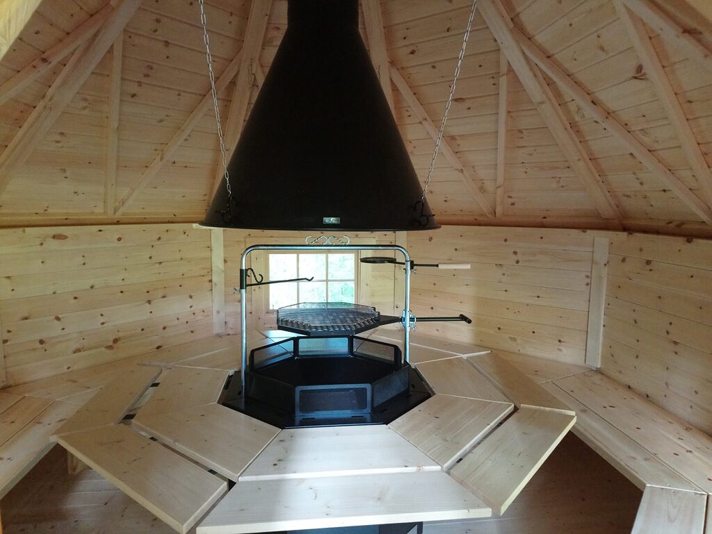 Innenraum der Grillhütte mit Grill in der Mitte und Sitzbänken