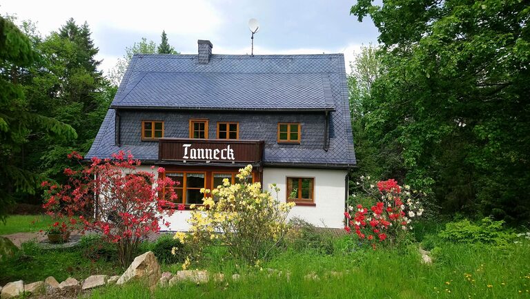 Ferienhaus Tanneck, Vorderansicht im Sommer mit blühenden Sträuchern