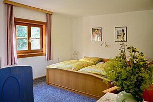 Schlafzimmer mit Doppelbett, gelber Bettwäsche und Blumenstrauß
